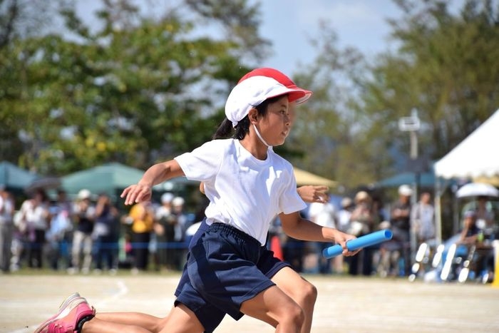 運動会でリレーのバトンを持って走る子ども